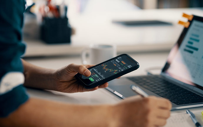 Person checking their investments with their phone and laptop.